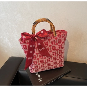 Close-up of red woven bridal tote bag with natural bamboo handles and silk bow detailing