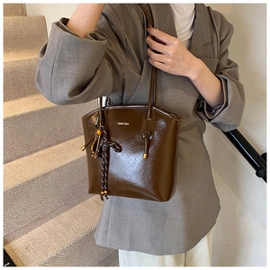 Détail du sac à main en cuir verni marron foncé avec logo doré et pompon corde