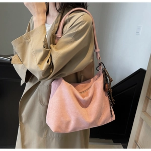 Detailed close-up of a pink suede hobo bag with fringe tassel on a khaki coat