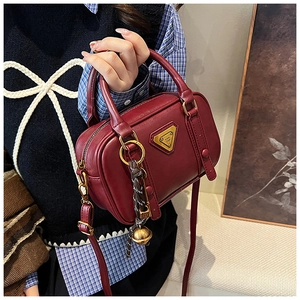 Detail view of burgundy leather Boston bag with metal logo and woven bell charm accessory
