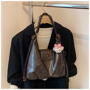 Detail of brown matte leather shoulder bag with gold clasp and pink bear charm decoration