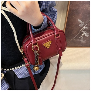 Detail einer dunkelroten Vintage-Tasche mit goldenem Dreieckslogo und geflochtenem Anhänger