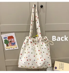 Back view of a white drawstring tote bag with colorful polka dots and a yellow charm