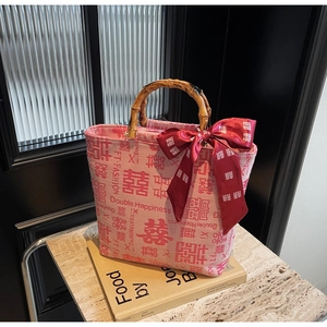Detail of a pink tote with bamboo handles, red ribbon, and Double Happiness pattern