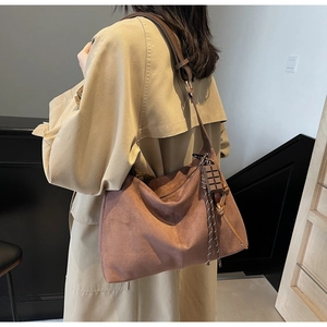 Brown suede hobo shoulder bag with chocolate pendant on a model in a beige coat