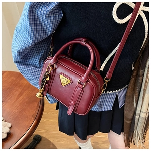 Detail of burgundy retro handbag with golden triangle plaque and adjustable strap
