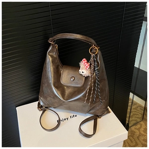 Macro detail of brown leather hobo bag with plush bear charm and adjustable straps