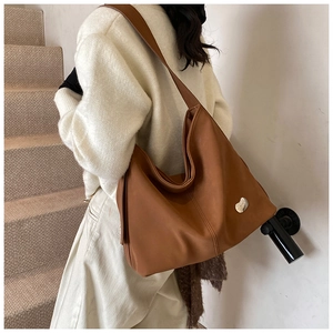 Close-up of a large brown hobo tote bag with a silver heart pendant on a soft leather surface