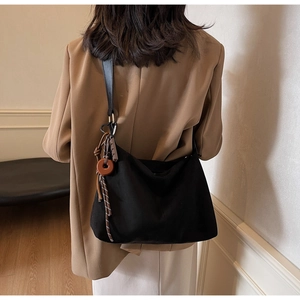 Detail of black canvas tote bag with woven pendant on model in chic blazer