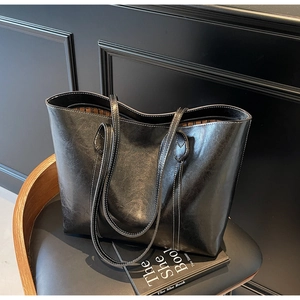 Detailed view of black tote bag showing premium glossy leather and white contrast stitching
