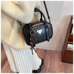 Detail of black crossbody bag with gold hardware and woven charm pendant on soft sweater