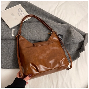 Detail shot of vintage brown oil-wax PU leather hobo bag on a grey coat background