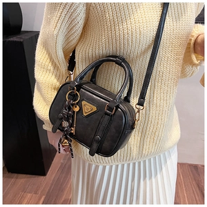 Detail of a vintage black leather crossbody bag with metal logo and stylish charm