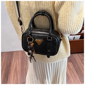 Detail view of a vintage black leather handbag with a gold triangle logo and tassel