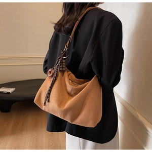 Brown suede hobo bag with tassel details shown on a model in a minimalist setting