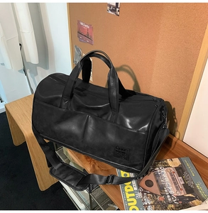 Detail of a black leather travel bag with sturdy handles and a padded shoulder strap on a table