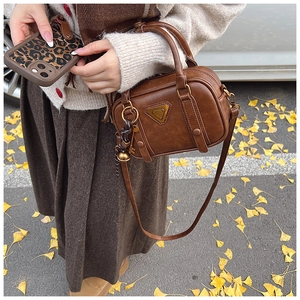 Detail of vintage brown leather bag with metal triangle plaque and leaf background