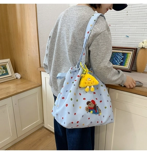 Detail of light blue polka dot nylon tote bag with drawstring and plush charm on model