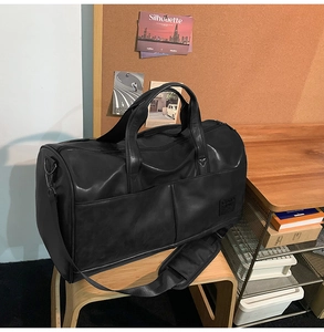 Close-up of black matte faux leather travel bag with shoulder strap on a wooden stool