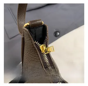 Macro shot of gold-tone metal zipper hardware on a dark brown lychee texture leather bag
