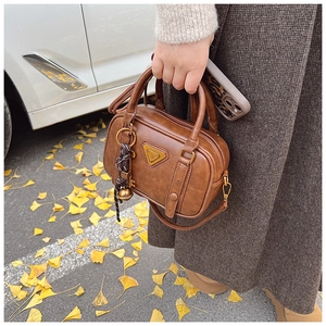 Detailed view of vintage brown leather square bag with gold bells and tassel on autumn street