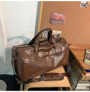 Detail of a dark brown leather duffel bag on a wooden bench with adjustable shoulder strap