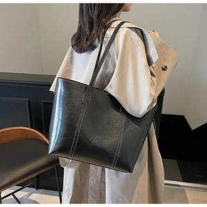 Macro detail of black tote bag showing white contrast stitching and glossy leather finish