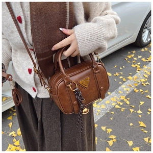 Close-up of a retro brown crossbody bag with metal logo and bell charm on autumn leaves