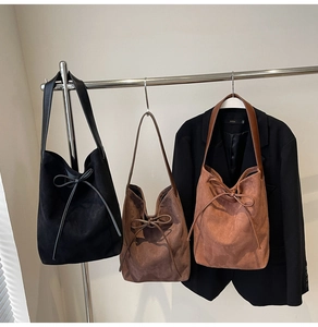 Close-up of suede tote bags with drawstring bow details in autumn colors on a metal rack