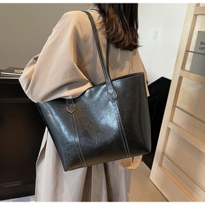 Macro shot of large black tote bag with white contrast stitching and shiny PU leather texture