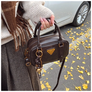 Detailed view of a dark brown retro handbag with metallic triangle logo and autumn charm