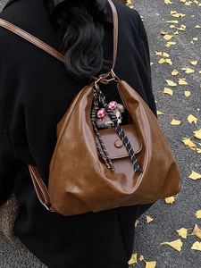Brown vintage faux leather backpack with woven strap and cute plush charm on ginkgo background