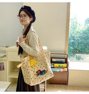 Detail of cream canvas tote bag with polka dots, dog embroidery, and plush pendant