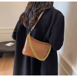 Detail einer braunen gesteppten Beuteltasche mit modischer Goldkette am Model