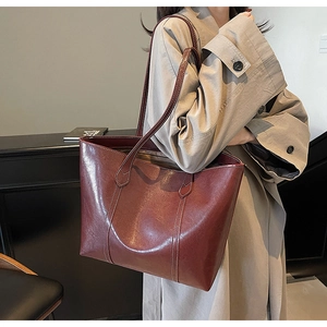 Detail view of burgundy leather tote bag with white contrast stitching on model