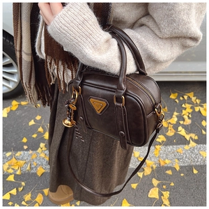 Detail of dark brown leather Boston bag with gold logo and tassel in autumn setting