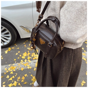 Detail of dark brown vintage crossbody bag with gold triangle logo and autumn leaves