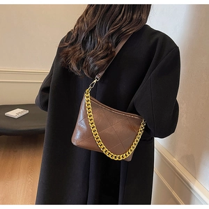 Detail einer braunen Stepp-Beuteltasche mit goldener Kette auf einem schwarzen Mantel