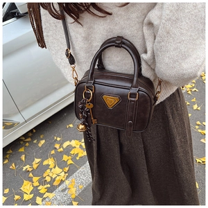 Detail einer braunen Vintage-Handtasche mit goldenem Logo, Schlüsselanhänger und Quasten