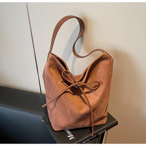 Detailed close-up of brown suede bucket bag with decorative bow tie on a sofa