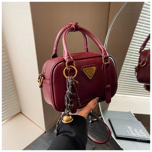 Detailansicht der weinroten Mini-Handtasche mit goldenem Logo und Glockenanhänger