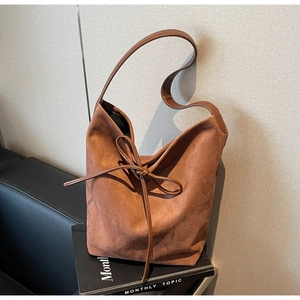 Detail of a brown vintage tote bag showing soft suede texture and leather bow tie decoration