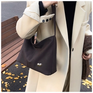 Detail of a dark coffee faux leather tote with a gold bean-shaped buckle in autumn setting
