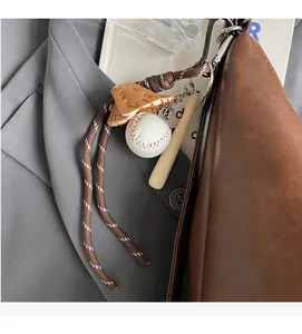 Dettaglio di ciondolo da baseball con mazza in legno e mini guanto su borsa tote in pelle