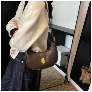 Close-up of brown crescent saddle bag featuring litchi grain texture and gold metal buckle