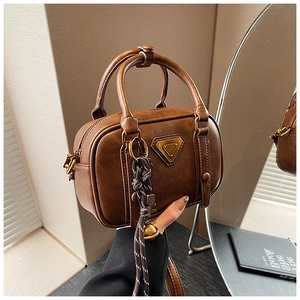 Detailaufnahme der braunen Vintage-Handtasche mit Metalldreieck-Logo und gewebtem Anhänger