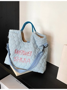 Light blue quilted tote bag with pink embroidery and circular handles on a wooden table