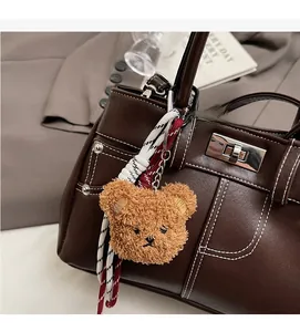 Close-up of a brown fluffy bear charm attached to a leather handbag with white stitching