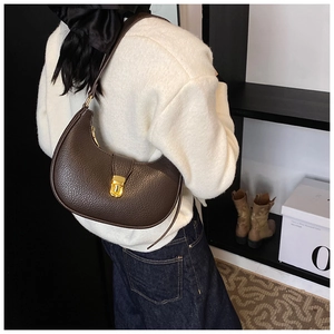 Detailed view of deep brown leather crescent bag with gold twist lock on shoulder