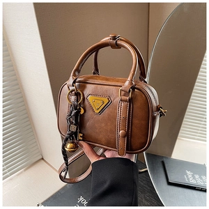 Details einer braunen Vintage-Handtasche mit goldener Plakette und Fransenanhänger